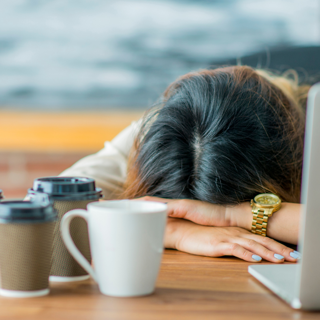 women slumped at her desk next to coffee cups and computer
